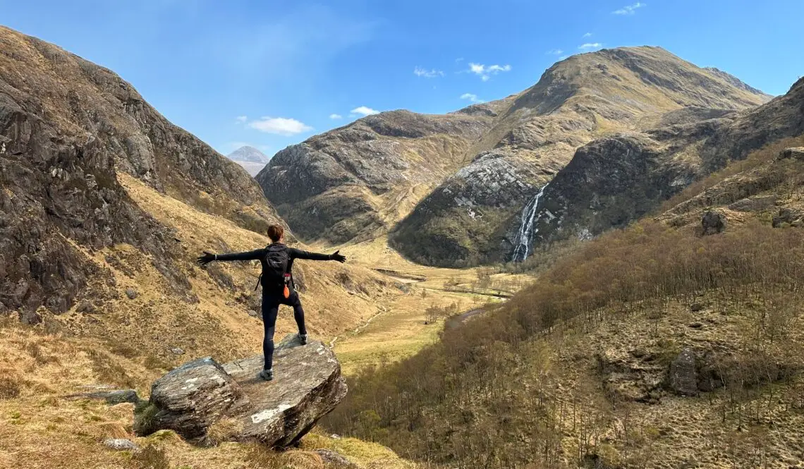 Terri standing on a rock with arms outstretched in the mountains near Steall Falls